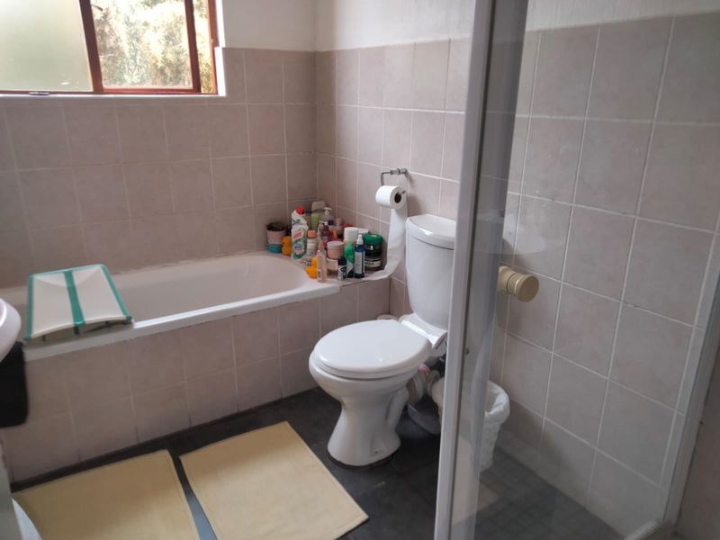 A functional bathroom featuring a bathtub, a separate shower enclosure, and a toilet, finished with neutral ceramic wall tiles and dark floor tiles.