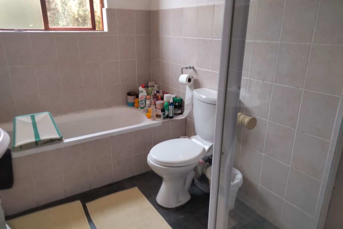 A functional bathroom featuring a bathtub, a separate shower enclosure, and a toilet, finished with neutral ceramic wall tiles and dark floor tiles.