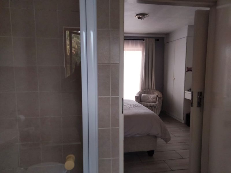 A bedroom view from an adjacent bathroom, featuring built-in cupboards and tiled flooring, with natural light entering through a window.