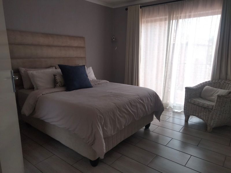 A well-lit bedroom featuring tiled flooring and a large sliding glass door with curtains providing access to the exterior.