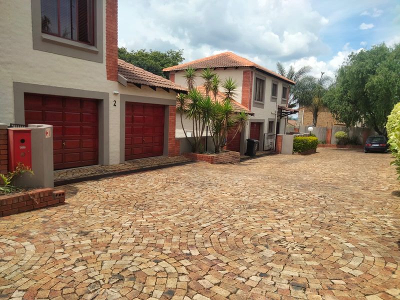 Front exterior view of a townhouse complex featuring a double garage, brick facade, and a circular pattern paved driveway.