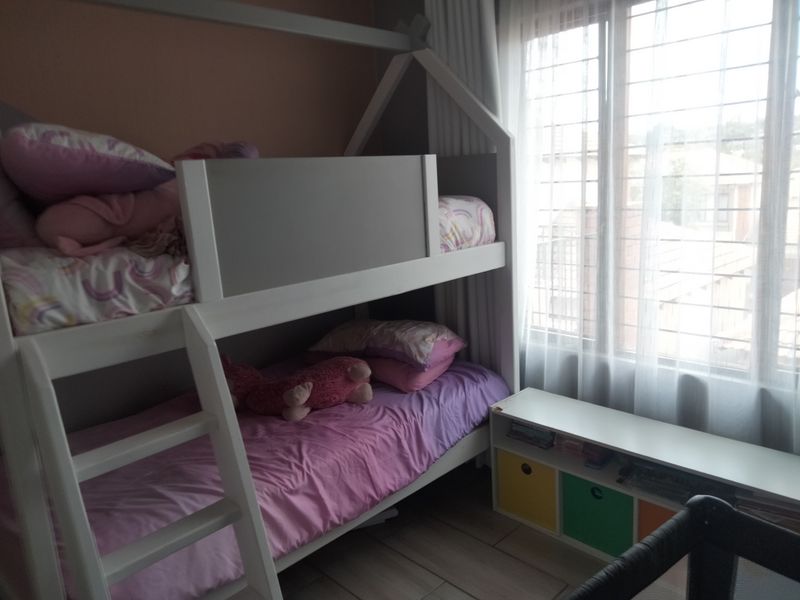 A bedroom featuring tiled flooring and a large window with security bars, providing natural light to the space.