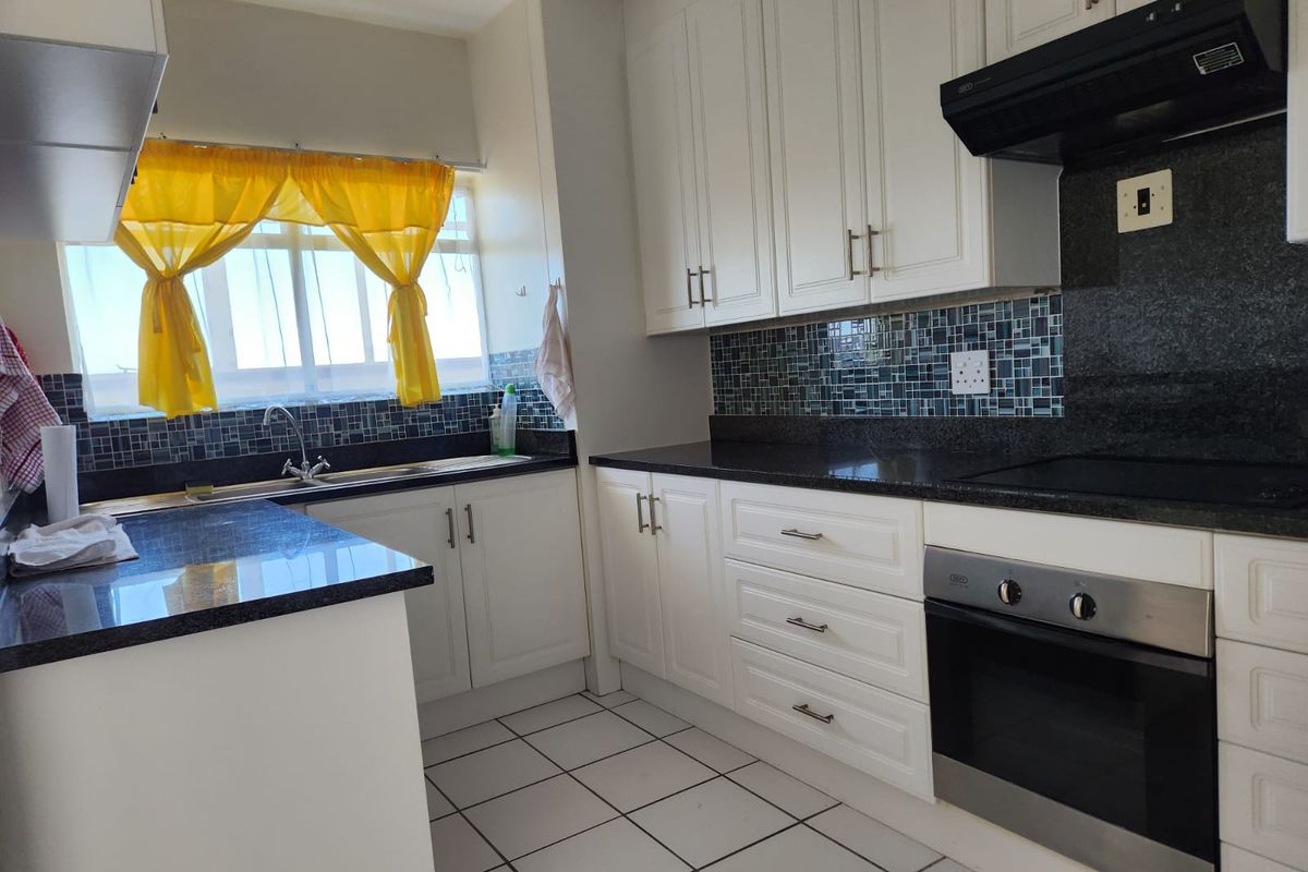 A functional kitchen featuring white cabinetry, dark granite countertops, a mosaic tile backsplash, and built-in oven with extractor fan.