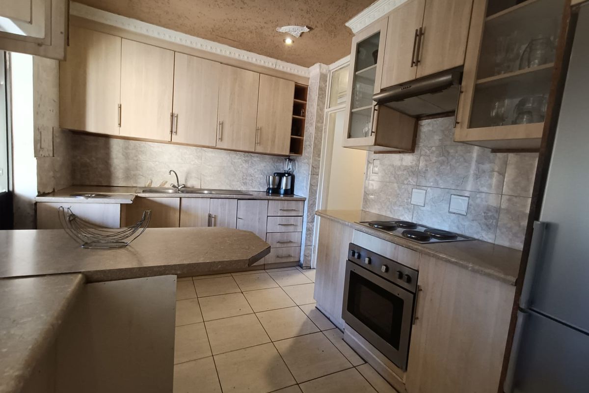 Functional kitchen featuring light wood cabinetry, built-in oven, electric hob, extractor fan, and tiled flooring with a breakfast bar area.