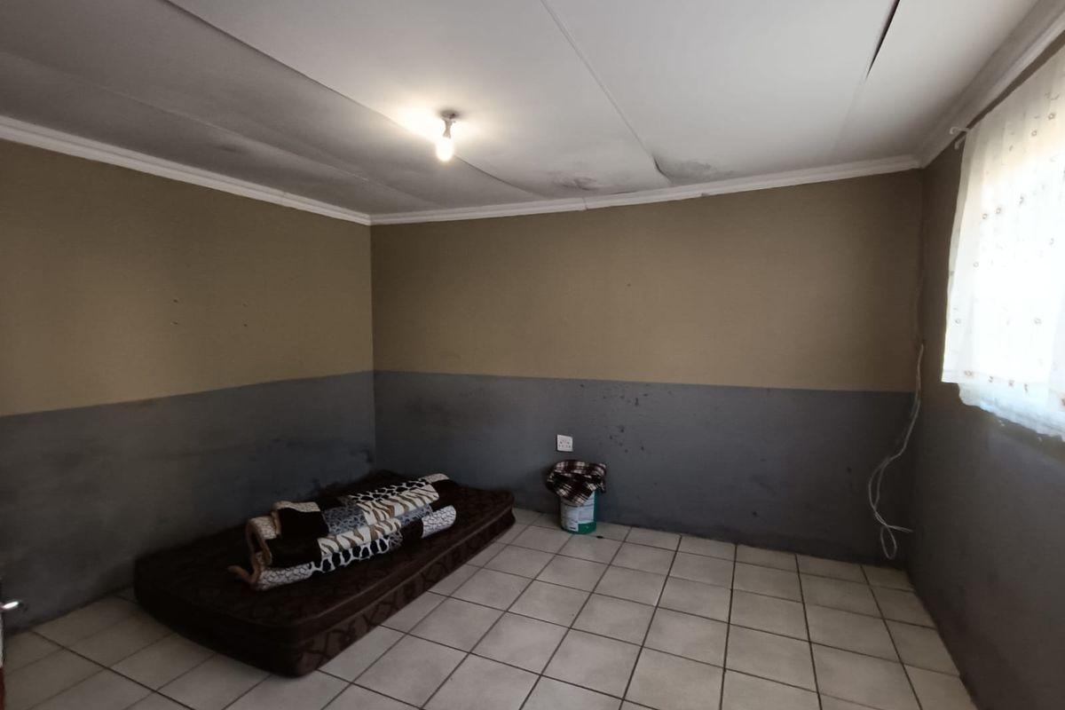 A bedroom featuring tiled flooring, two-tone painted walls, and a ceiling showing signs of water damage and structural cracking.