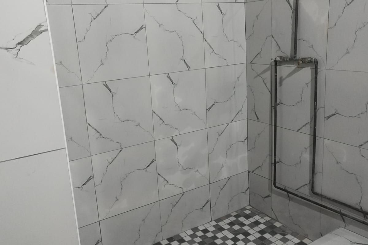 A modern walk-in shower featuring marble-effect wall tiles and a contrasting mosaic tiled floor with an exposed chrome shower fixture.
