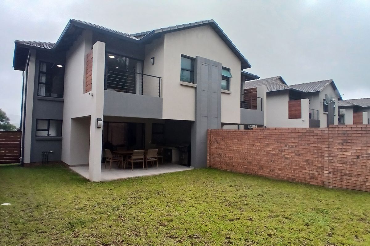 Rear view of a modern townhouse featuring a covered patio with built-in braai, an upper-level balcony, and a private enclosed garden area.