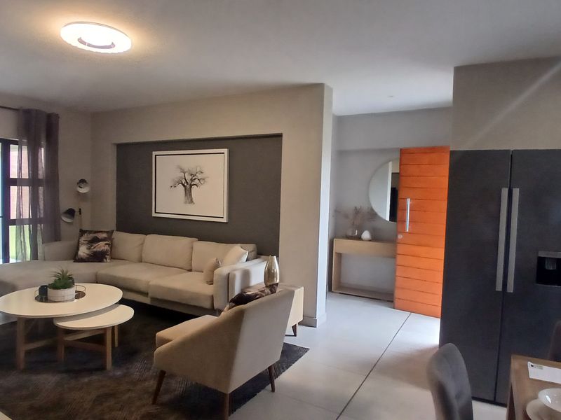 A bright open-plan living area featuring modern tiled flooring, a feature wall, and seamless access to an outdoor patio through sliding glass doors.