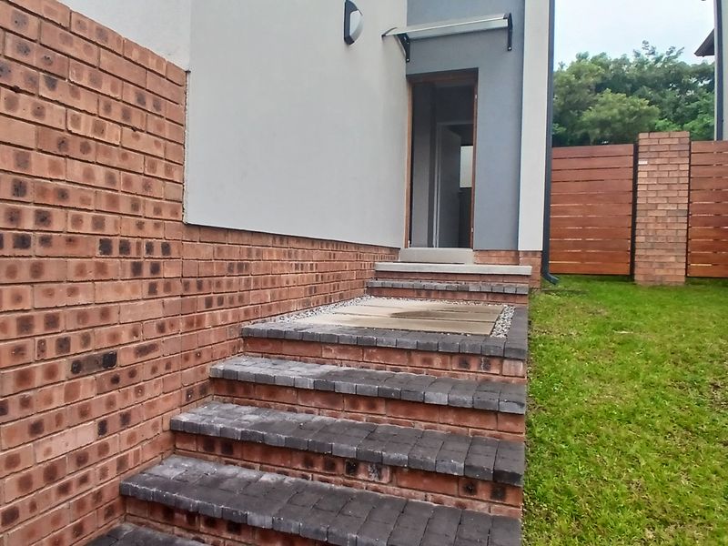 Rear exterior view of the townhouse featuring brick steps leading to a doorway, complemented by a timber privacy screen and landscaped garden area.