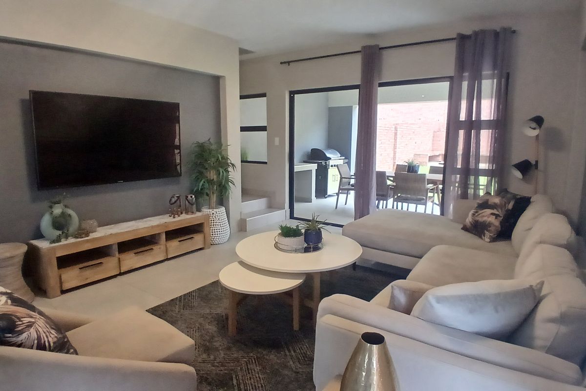 Spacious living room featuring tiled floors, a modern recessed wall for media, and large sliding glass doors providing seamless access to the outdoor patio area.