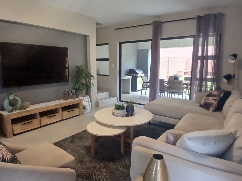 Spacious living room featuring tiled floors, a modern recessed wall for media, and large sliding glass doors providing seamless access to the outdoor patio area.