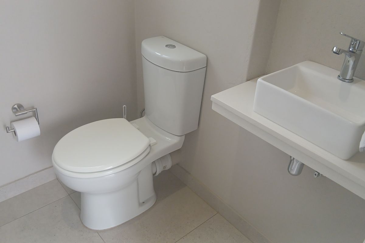 A clean, modern guest bathroom featuring a white toilet, a floating vanity shelf with a vessel sink, and neutral floor tiles.