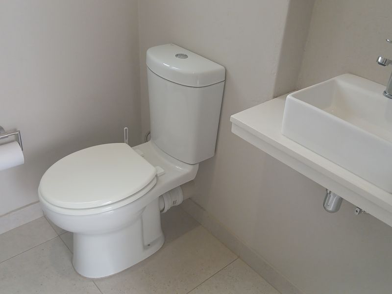 A clean, modern guest bathroom featuring a white toilet, a floating vanity shelf with a vessel sink, and neutral floor tiles.