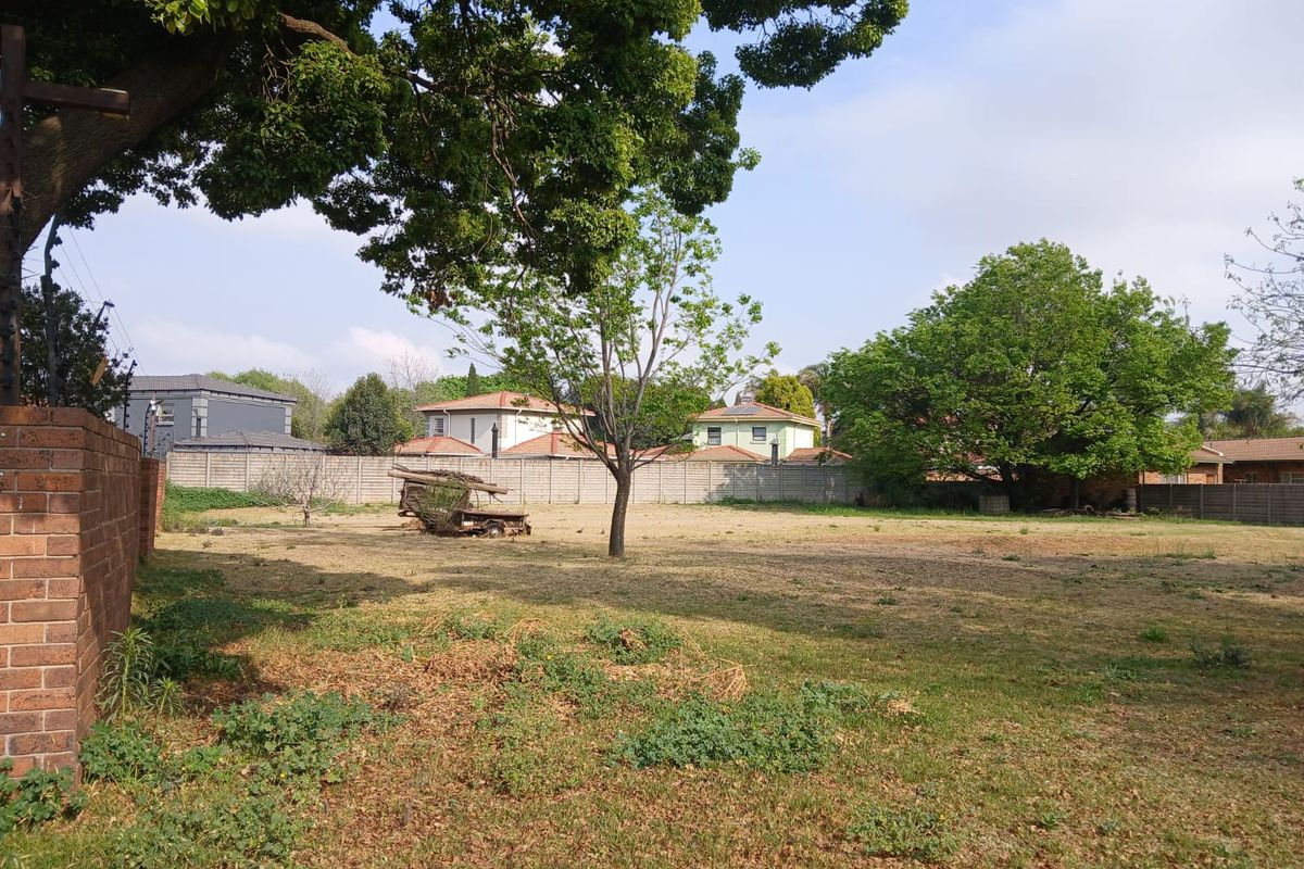 A vacant residential plot featuring established trees, perimeter brick walling, and clear boundaries, offering a blank canvas for future development.