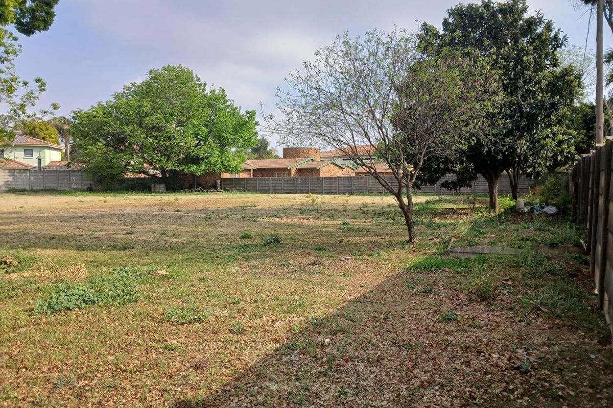 A spacious, level residential vacant land plot featuring established trees and perimeter boundary walling, offering a blank canvas for future development.