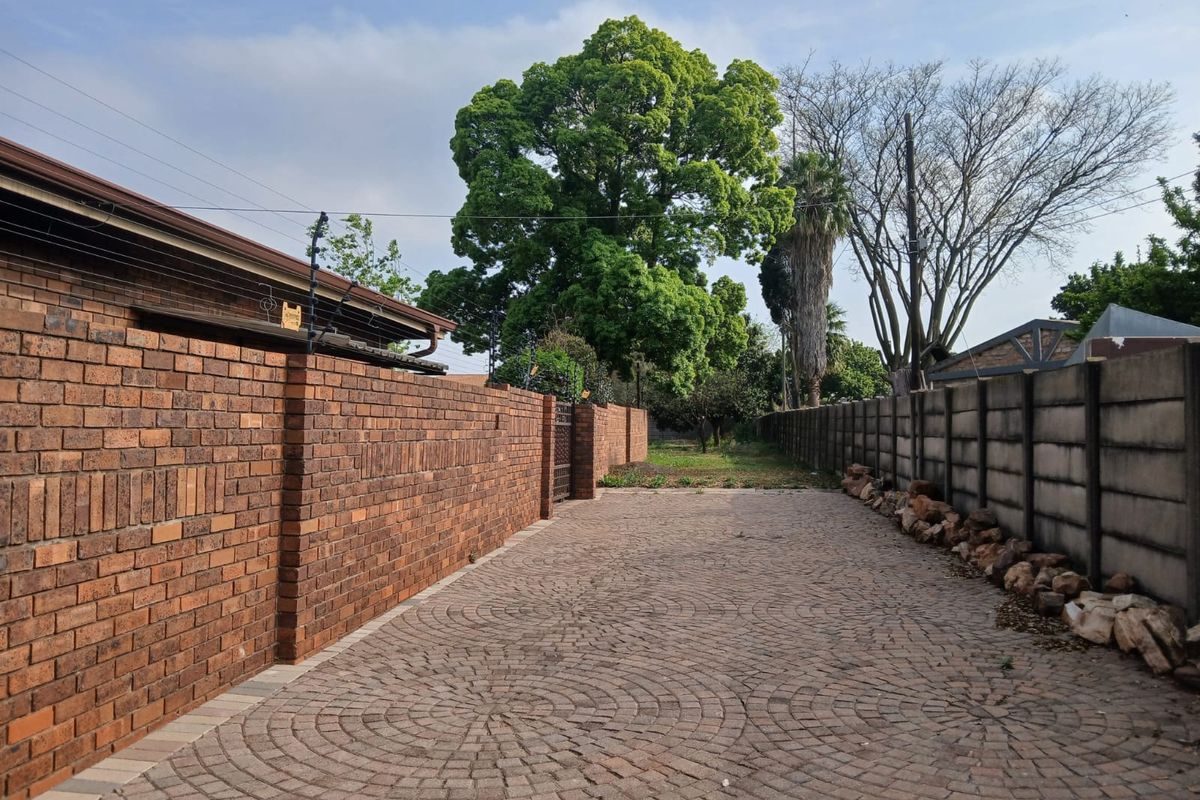 A paved driveway leading towards the rear of the property, enclosed by brick and concrete boundary walls with electric fencing.