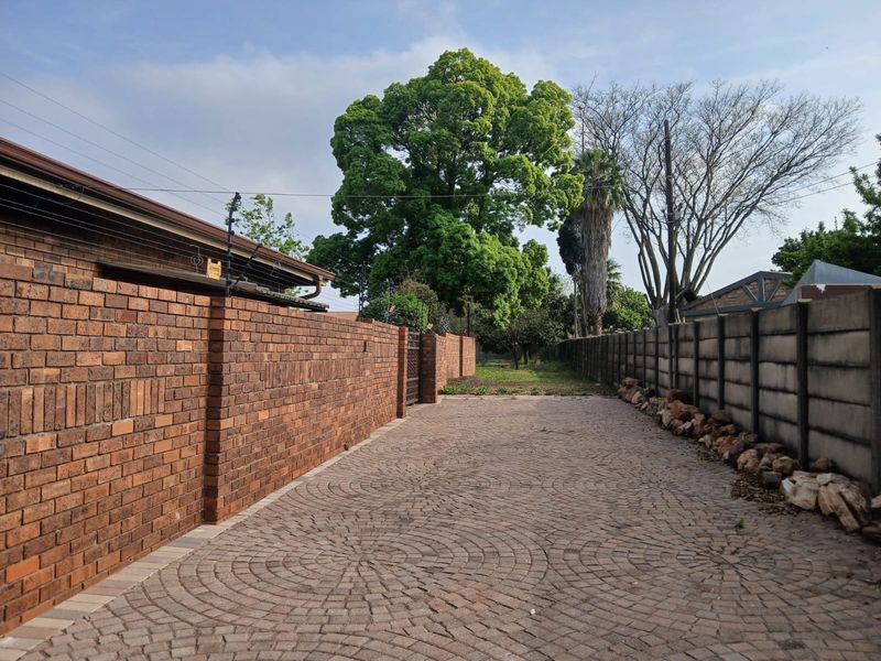 A paved driveway leading towards the rear of the property, enclosed by brick and concrete boundary walls with electric fencing.