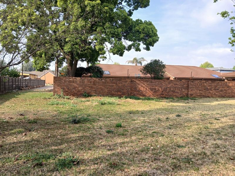 A vacant residential plot featuring established trees and a perimeter brick boundary wall, offering a blank canvas for future development.