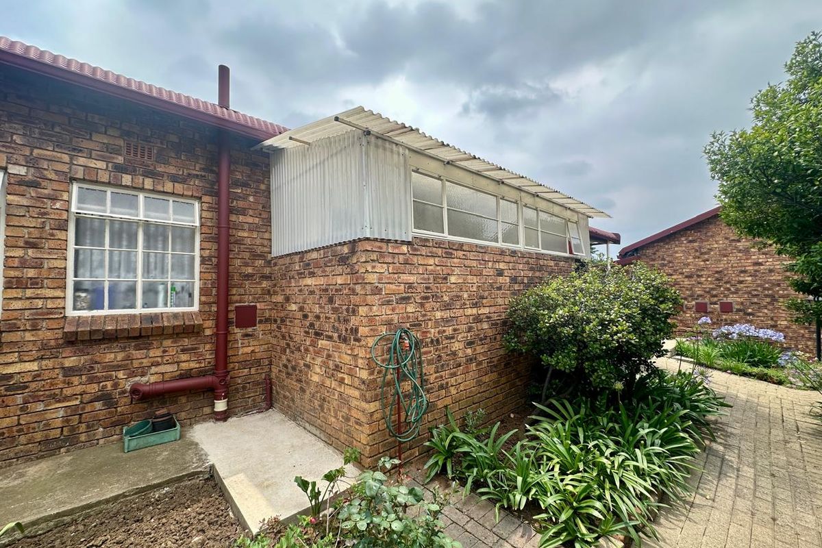 Exterior view of the rear brick facade featuring a lean-to structure with corrugated roofing and paved garden pathway.