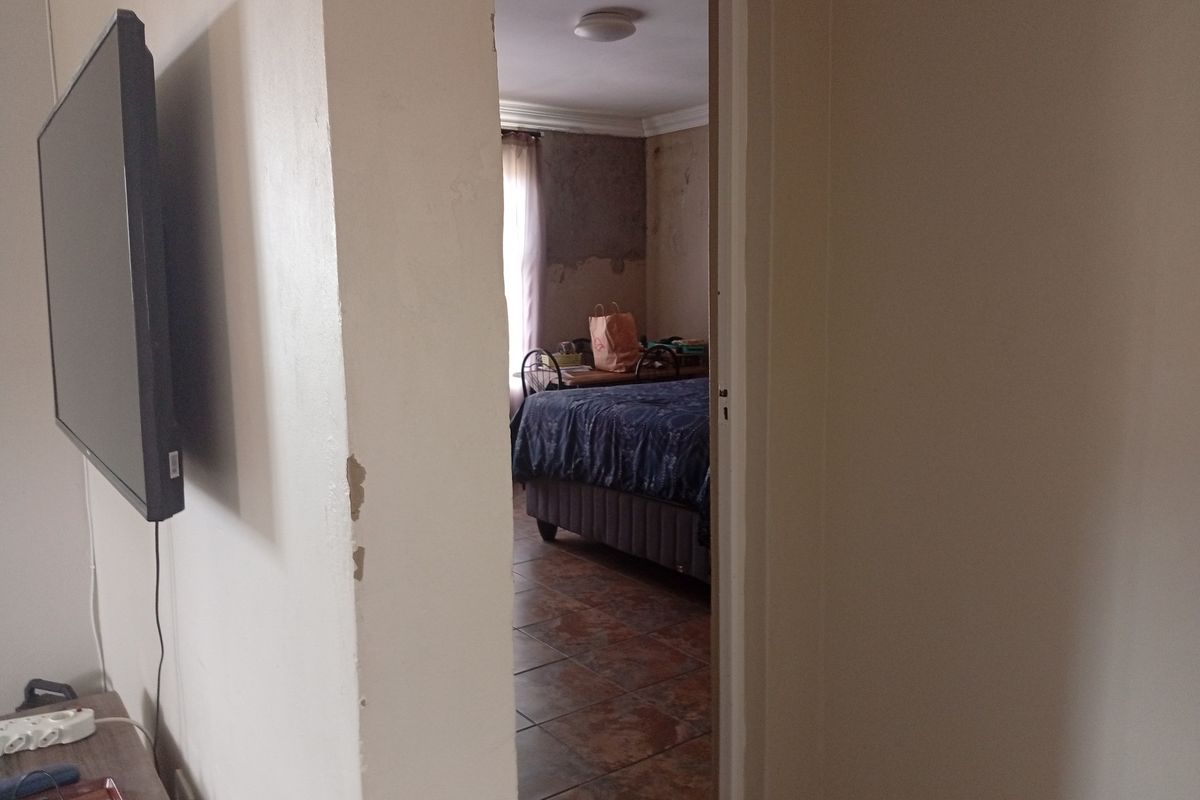 A view through a doorway into a bedroom featuring tiled flooring and visible wall surface damage requiring repair and redecoration.
