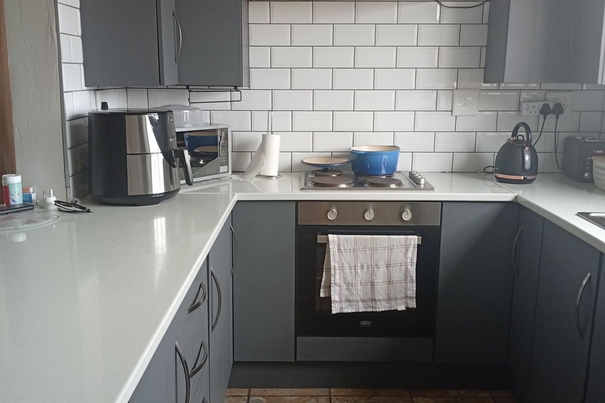 A modern kitchen featuring grey cabinetry, white stone countertops, a subway tile backsplash, and a built-in oven with an extractor fan.