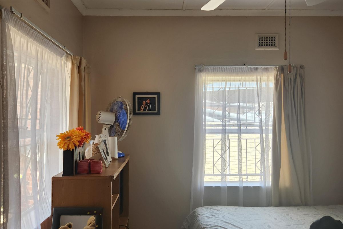 A bedroom featuring a ceiling fan, wall-mounted air conditioning unit, and security bars on the windows.