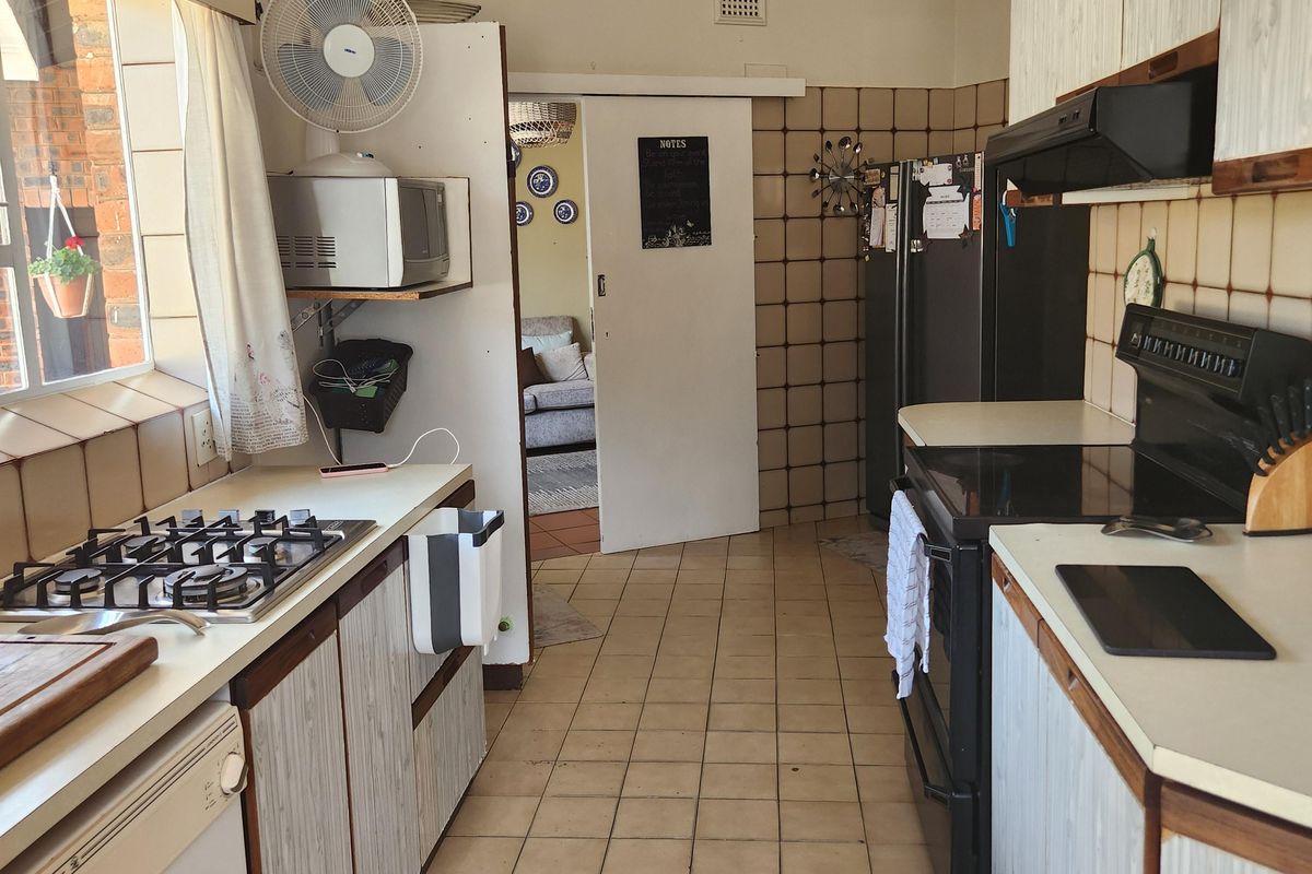 A functional kitchen featuring tiled flooring, built-in cabinetry, a gas hob, and an integrated oven, with a sliding door leading to the living area.