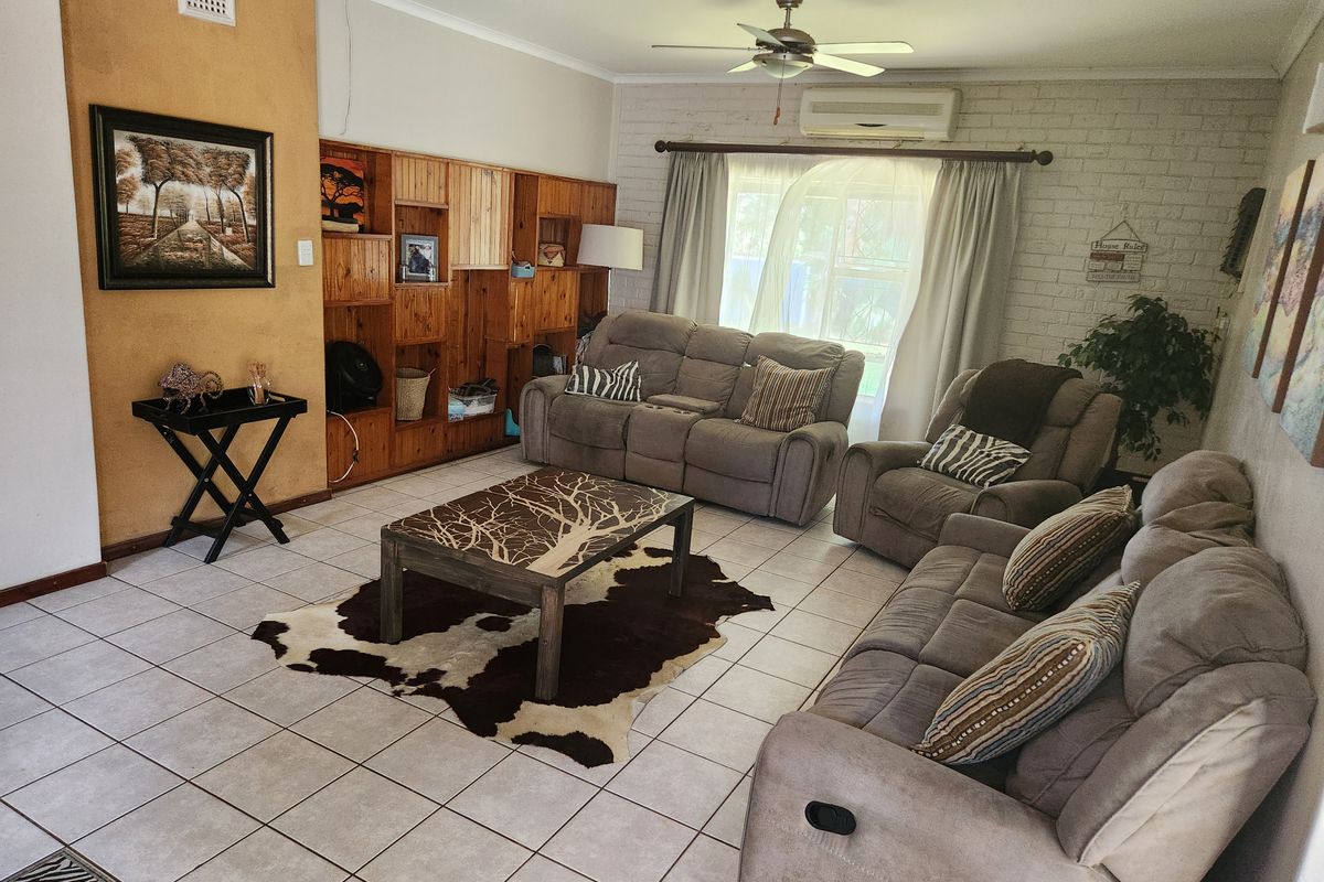 A spacious living room featuring tiled flooring, a built-in wooden shelving unit, a ceiling fan, and a wall-mounted air conditioning unit.