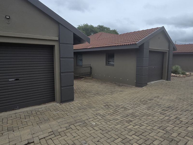 A row of townhouse garages featuring modern roller shutter doors, tiled roofs, and a well-maintained paved driveway area.