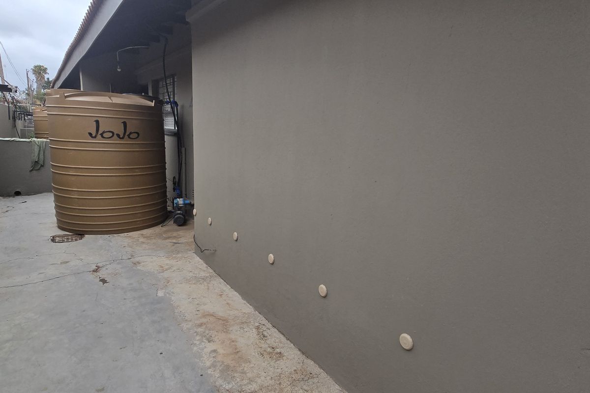 Side exterior area featuring a water storage tank, pump system, and concrete paving along the building wall.