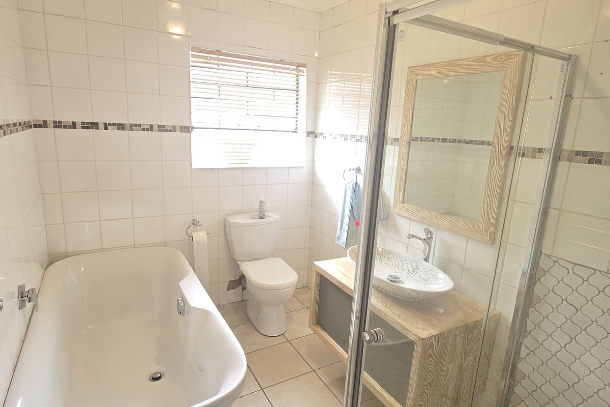 A functional bathroom featuring a freestanding bathtub, a separate glass-enclosed shower, a vanity with a vessel sink, and neutral ceramic tiling throughout.