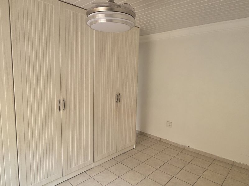 A clean, empty bedroom featuring extensive built-in cupboards, tiled flooring, and a ceiling fan, offering a neutral canvas for personalization.