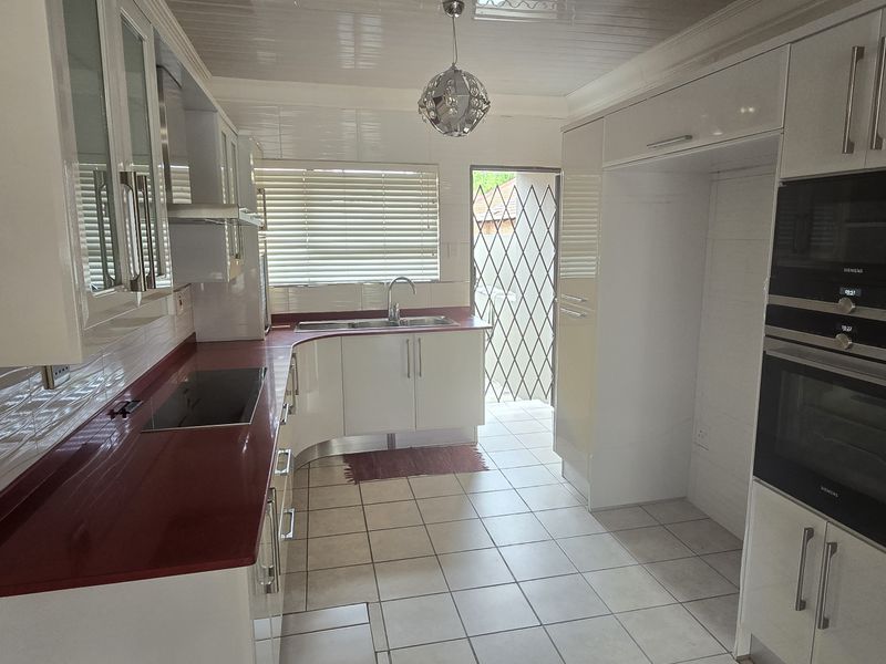 A clean, modern kitchen featuring high-gloss cabinetry, integrated appliances, a red countertop, and tiled flooring with direct access to the exterior.