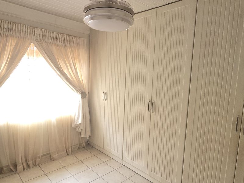 A bright bedroom featuring extensive built-in cupboards, neutral tiled flooring, and a central ceiling light fixture.