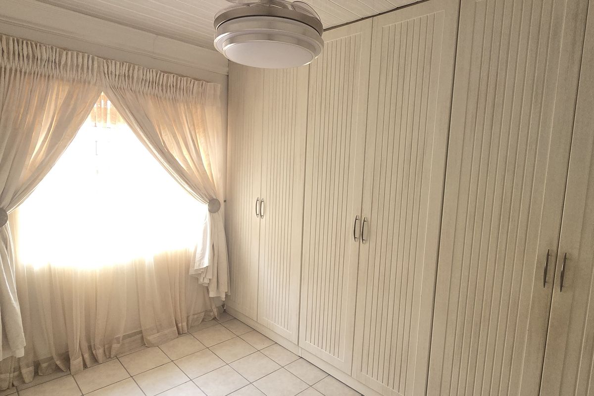 A bright bedroom featuring extensive built-in cupboards, neutral tiled flooring, and a central ceiling light fixture.