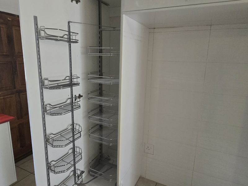 A functional kitchen area featuring a stainless steel sink, tiled splashback, and a convenient pull-out pantry unit, offering a practical layout for food preparation.