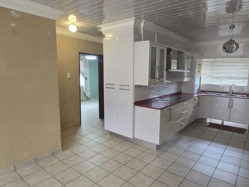A functional kitchen featuring white cabinetry, red countertops, tiled flooring, and a coved ceiling, offering a clean and practical workspace.