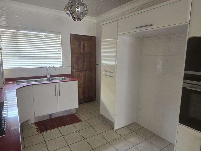 A clean, functional kitchen featuring white cabinetry, red countertops, built-in Siemens appliances, and tiled flooring with a window providing natural light.