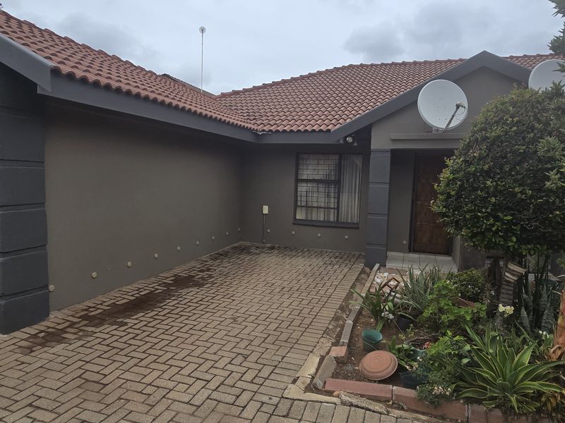 Front elevation of a townhouse featuring a paved driveway, single garage, and tiled roof with established garden beds.