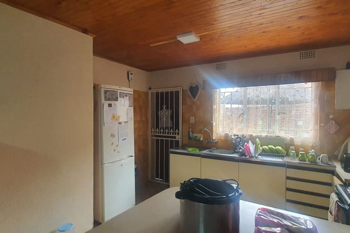A functional kitchen featuring timber ceiling paneling, tiled splashbacks, and built-in cabinetry with a stainless steel sink and window view.
