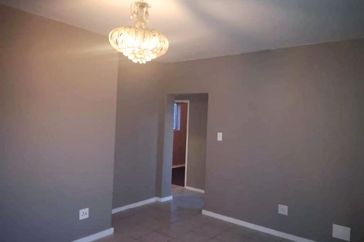 A neutral-toned living area featuring tiled flooring and a central light fixture, leading through to an adjacent room.