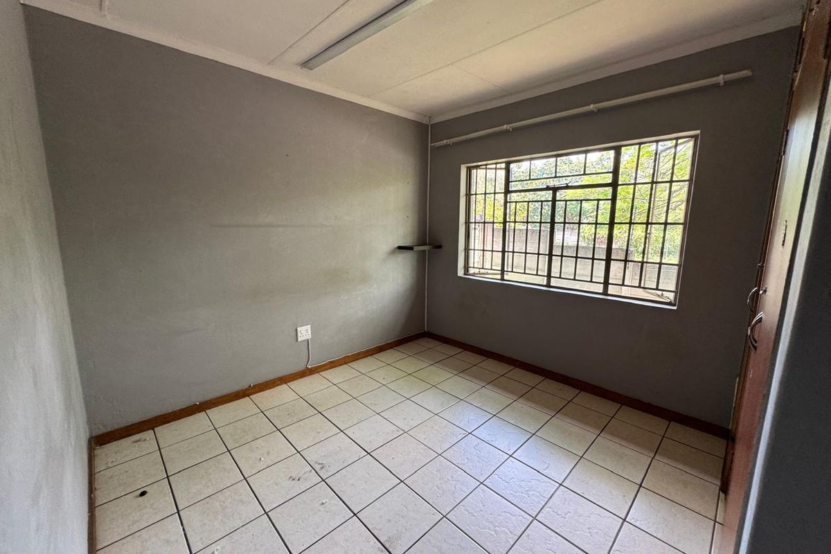 An empty bedroom featuring tiled flooring, burglar bars on the window, and neutral grey walls, providing a blank canvas for renovation or staging.