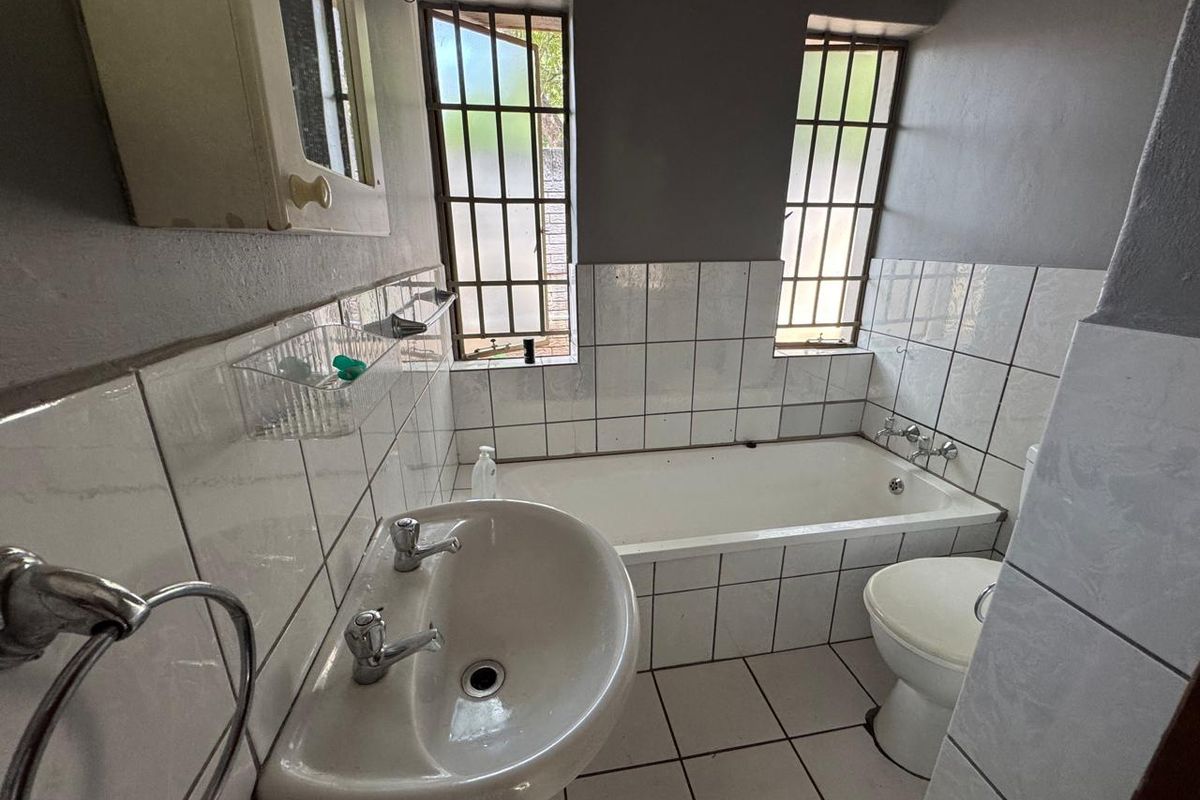 A functional bathroom featuring a pedestal basin, built-in bathtub, and toilet, finished with ceramic tiling and security bars on the windows.
