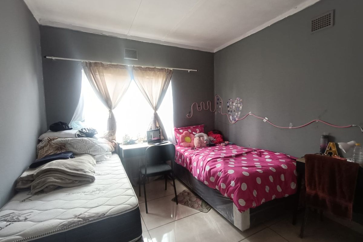 A functional bedroom featuring tiled flooring, built-in wall vents, and a window with curtain rod, providing a practical living space.