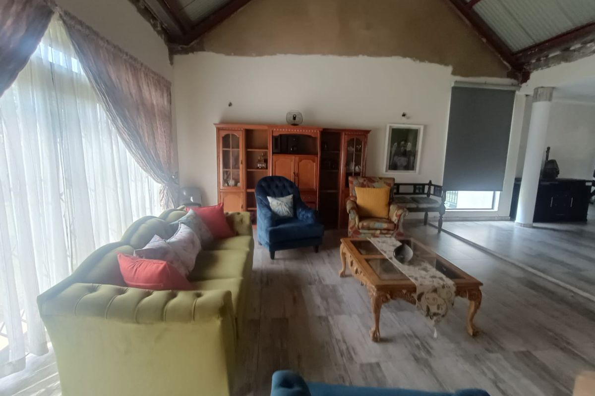 Spacious living area featuring high vaulted ceilings with exposed beams, wood-look tile flooring, and large windows providing ample natural light.