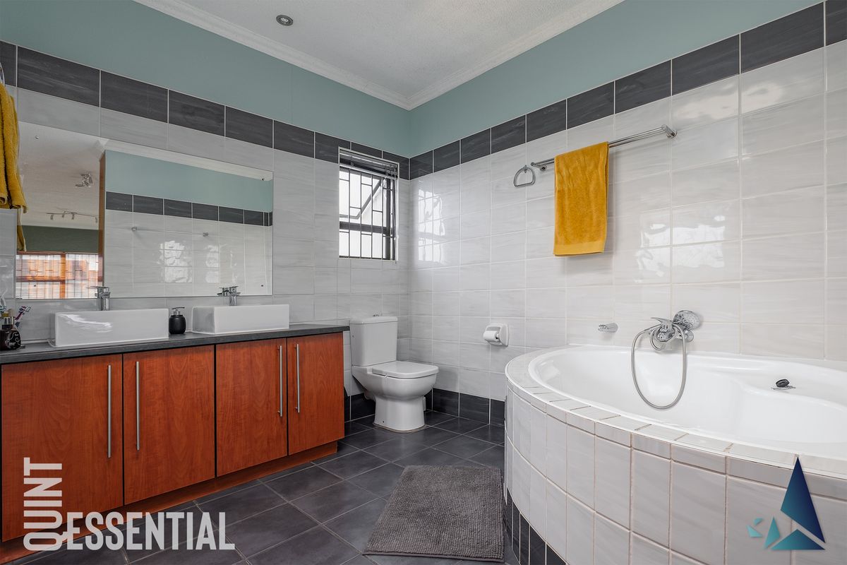 A well-maintained bathroom featuring a double vanity with vessel sinks, a tiled bathtub, and a separate toilet.