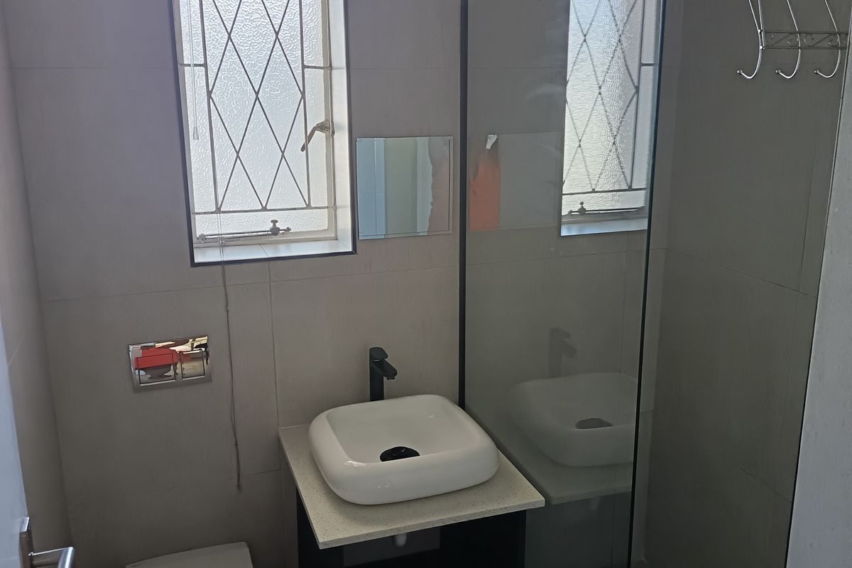 Modern bathroom featuring a wall-mounted toilet, vessel sink on a vanity cabinet, and a glass-enclosed shower with a rain shower head.