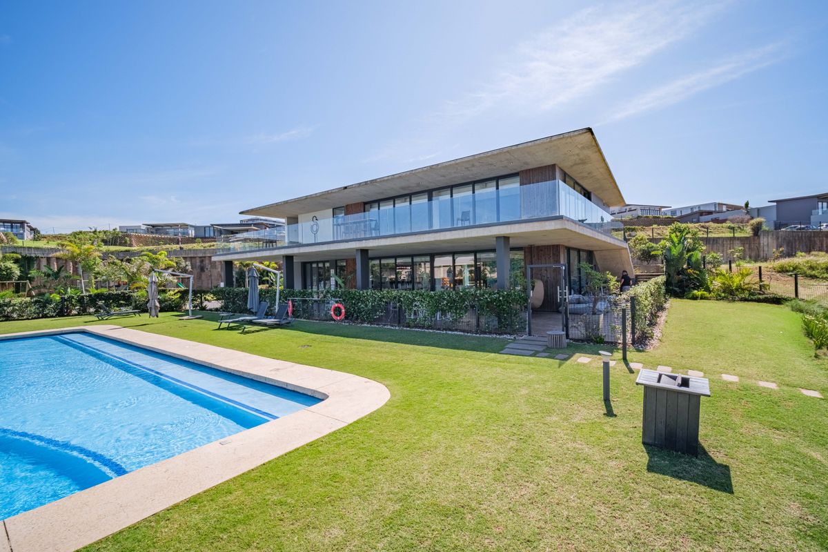 A modern two-story residence featuring a swimming pool, landscaped lawn, and expansive glass balconies, showcasing contemporary architectural design and outdoor living space.