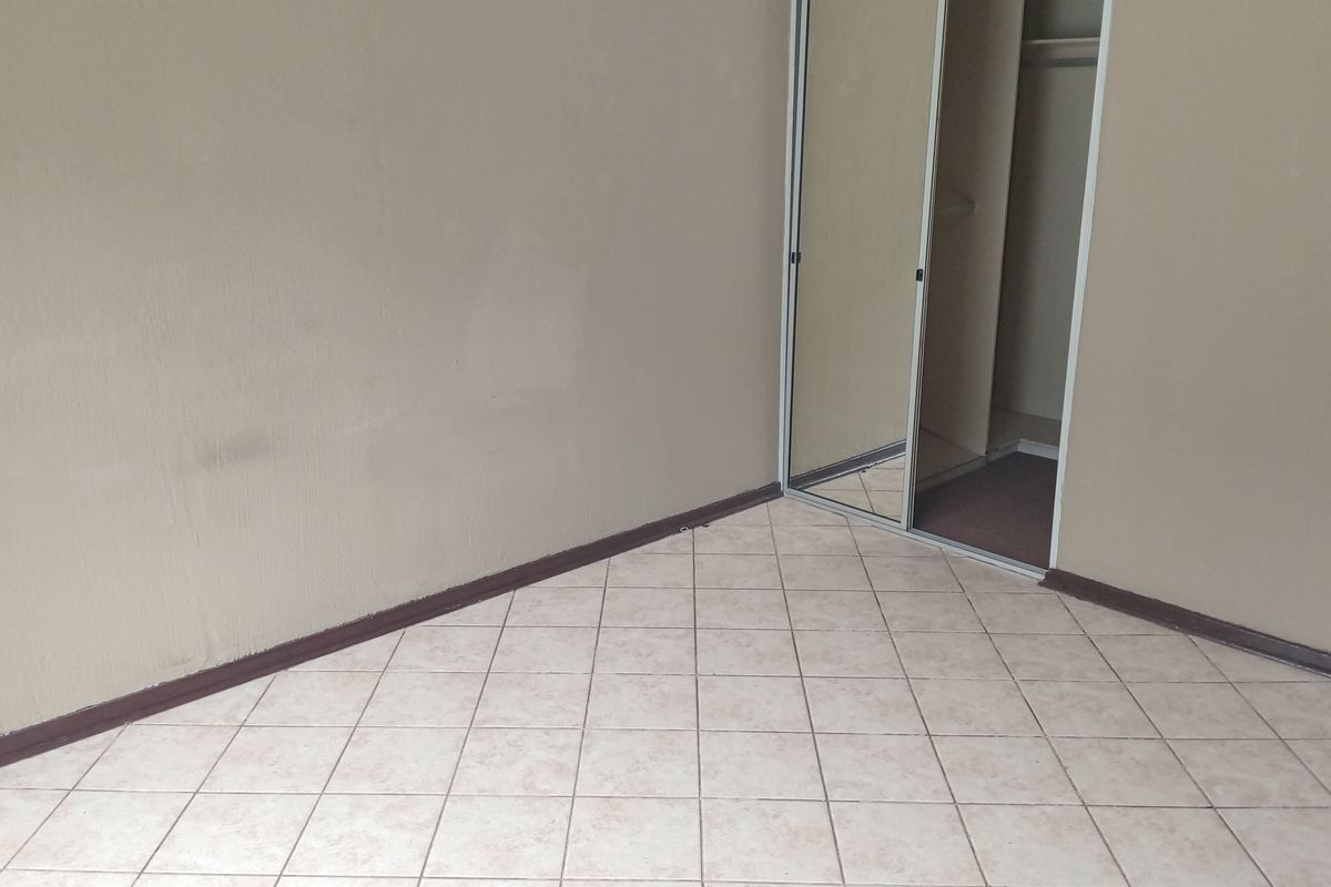 A vacant bedroom featuring neutral tiled flooring and a built-in wardrobe with mirrored sliding doors.