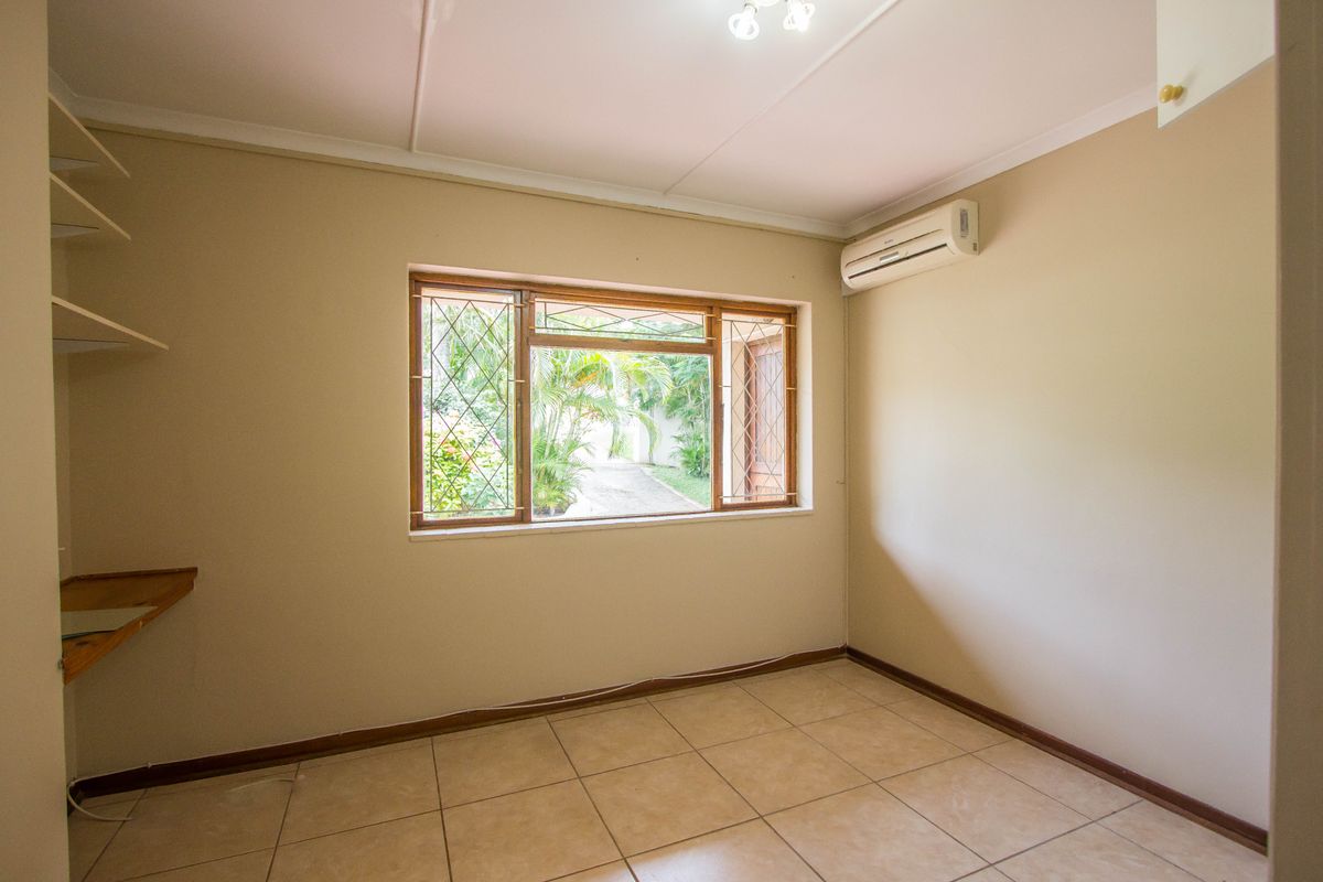 A bright, empty bedroom featuring tiled flooring, built-in shelving, and a wall-mounted air conditioning unit overlooking the garden.